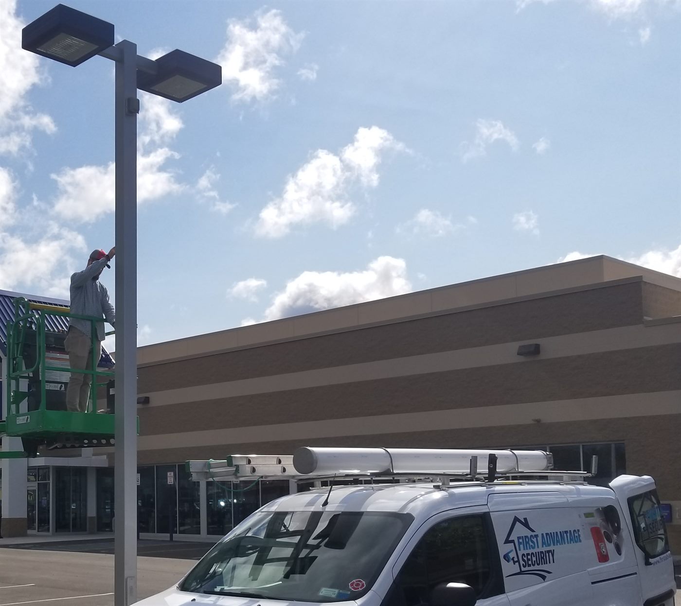 A First Advantage technician on a boom lift fitting a camera to a parking-lot light pole, with the branded van parked below